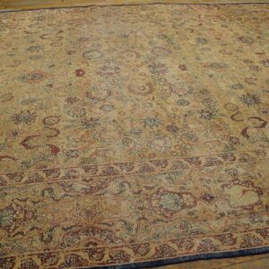 Distressed low-pile rug with tan field and complex floral pattern in red, rust, and navy blue on wood floor.