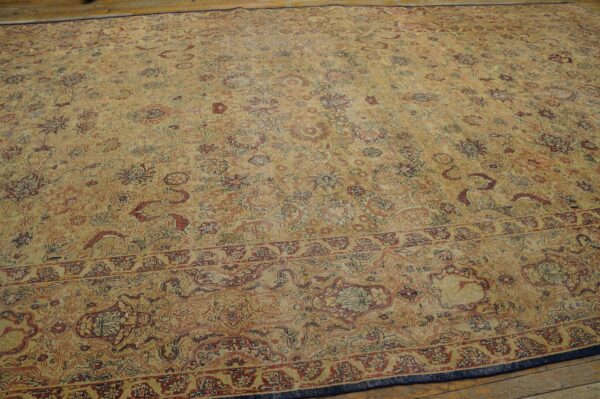 Distressed low-pile rug with tan field and complex floral pattern in red, rust, and navy blue on wood floor.