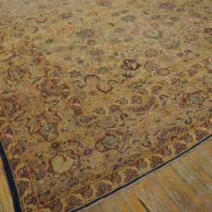 Low pile rug in golden-beige with intricate red and navy floral patterns placed on worn wood flooring.