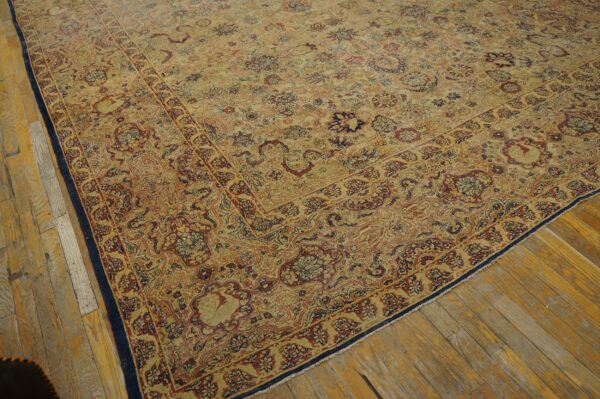 Low pile rug in golden-beige with intricate red and navy floral patterns placed on worn wood flooring.