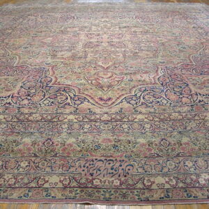 Low-pile rug with complex floral motifs in muted rose, beige, and indigo on a wood floor.