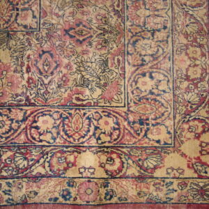 The corner of a traditional rug shows dense floral borders in faded red, dark blue, and beige.