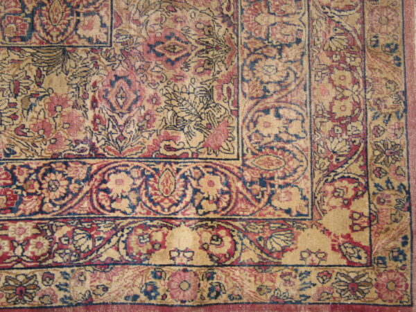 The corner of a traditional rug shows dense floral borders in faded red, dark blue, and beige.