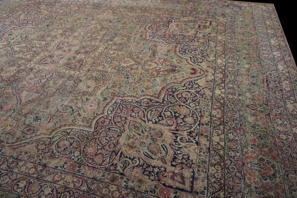 Angled view of a detailed beige, rose, and navy blue traditional rug showing a complex corner medallion.