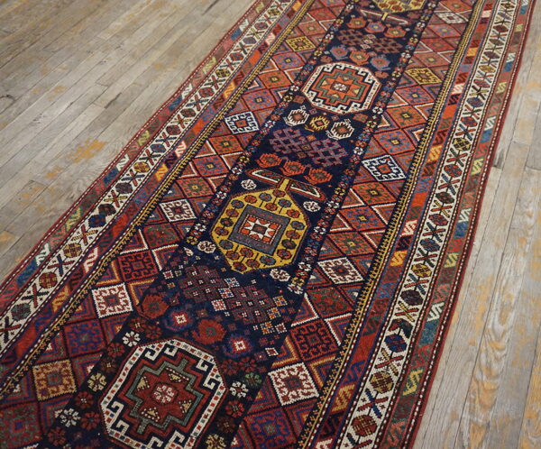 Geometric runner rug with a navy field and multicolored medallions resting on light weathered wood floorboards.
