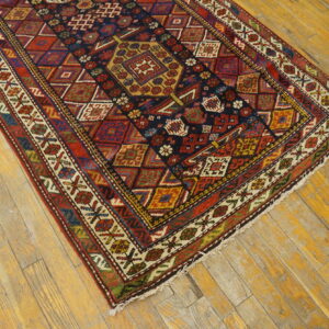 Detailed geometric rug in navy, red, and gold colors lying on weathered light hardwood flooring.