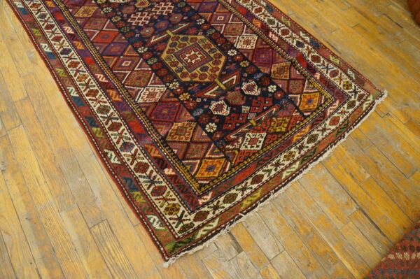 Detailed geometric rug in navy, red, and gold colors lying on weathered light hardwood flooring.