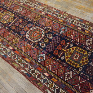 Multicolored geometric runner rug in rust, navy, and gold patterns displayed over light, distressed wood plank flooring.