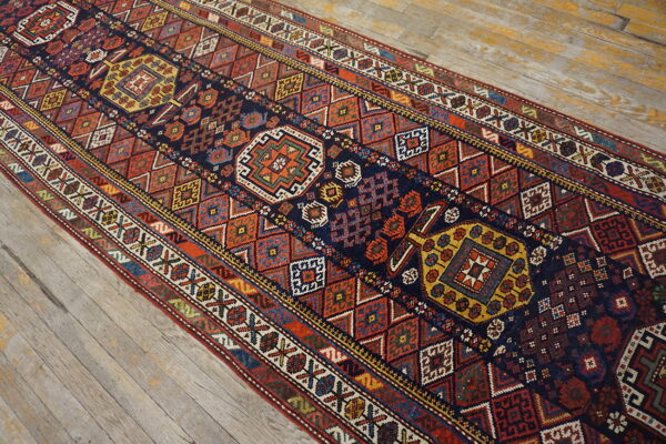 Multicolored geometric runner rug in rust, navy, and gold patterns displayed over light, distressed wood plank flooring.