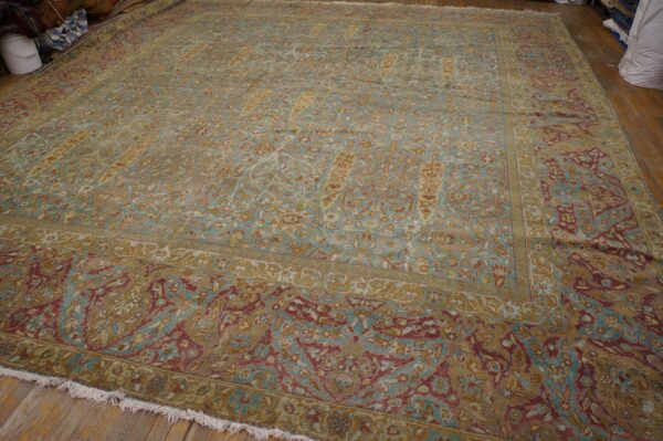Large antique rug in faded teal, gold, and maroon floral pattern resting on wood flooring.