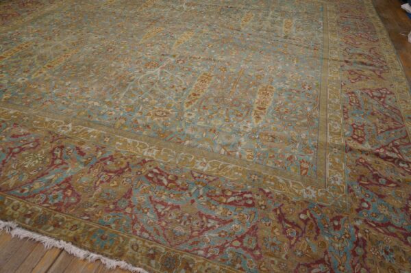 Large, traditional rug in teal, gold, and cranberry floral patterns resting on wooden floors.