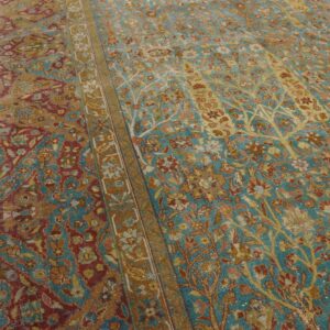 Faded floral rug in teal, gold, and rust with a central border, resting on wood planks.