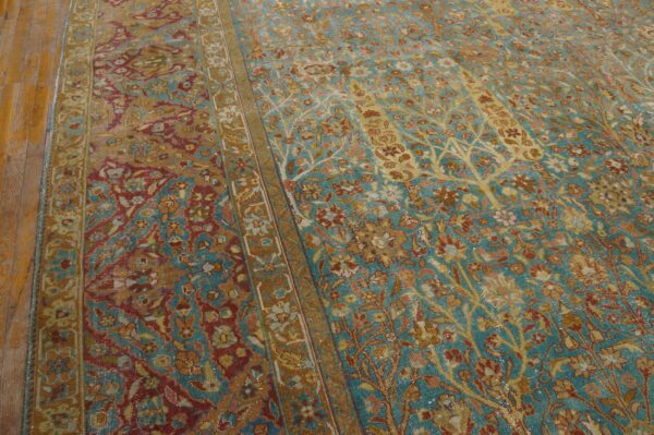 Faded floral rug in teal, gold, and rust with a central border, resting on wood planks.