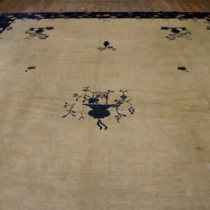 Large beige rug with dark blue stylized floral patterns and a wide navy border on wood flooring.