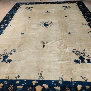 Beige rug with wide navy blue border and scattered blue floral vessels rests on tile.