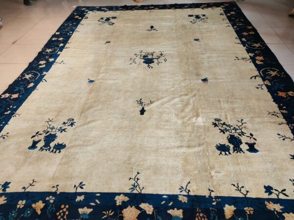 Beige rug with wide navy blue border and scattered blue floral vessels rests on tile.