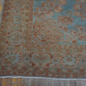 Ornate traditional rug in muted teal and terracotta on rustic yellow hardwood planks.