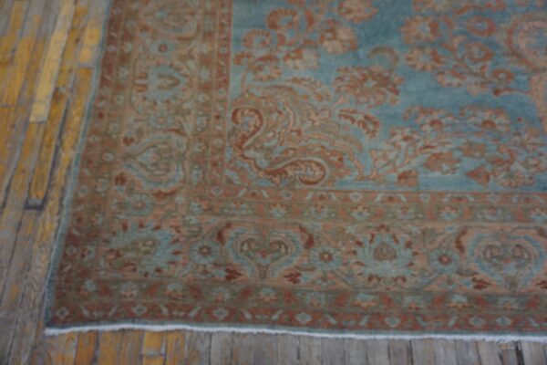 Ornate traditional rug in muted teal and terracotta on rustic yellow hardwood planks.