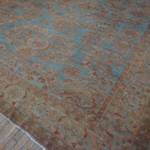 Teal and rust colored traditional patterned rug displayed diagonally on worn wooden floor planks.