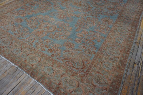 Teal and rust colored traditional patterned rug displayed diagonally on worn wooden floor planks.