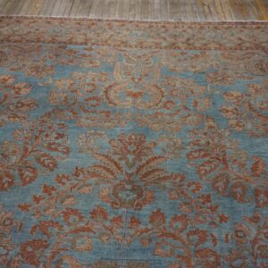 Dusty blue rug featuring a detailed red floral pattern and border on wide plank wood floors.