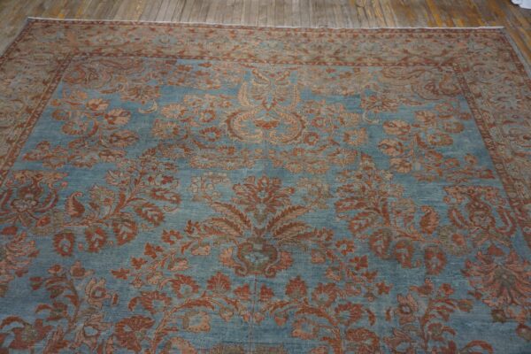 Dusty blue rug featuring a detailed red floral pattern and border on wide plank wood floors.