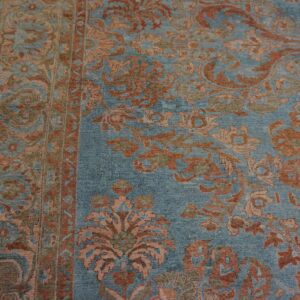 Muted blue rug detailed with rust and pale orange floral motifs next to worn, yellow wood flooring.