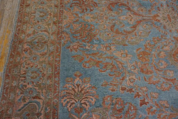 Muted blue rug detailed with rust and pale orange floral motifs next to worn, yellow wood flooring.