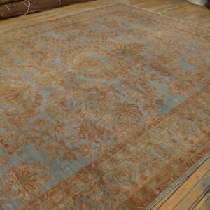 A heavily faded blue-gray rug featuring a large rust-colored floral pattern on distressed plank flooring.
