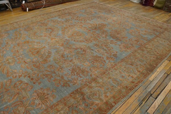 A heavily faded blue-gray rug featuring a large rust-colored floral pattern on distressed plank flooring.