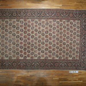 Beige rug with a dense paisley pattern and dark floral borders covers a honey-toned wood floor.