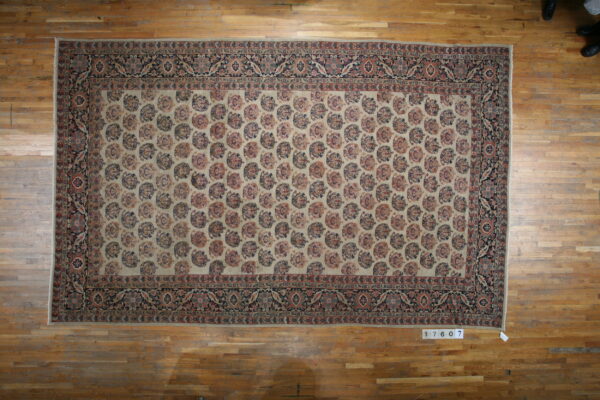Beige rug with a dense paisley pattern and dark floral borders covers a honey-toned wood floor.
