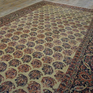 Beige rug with repeating red and navy paisley patterns and a dark floral border rests on wood planks.