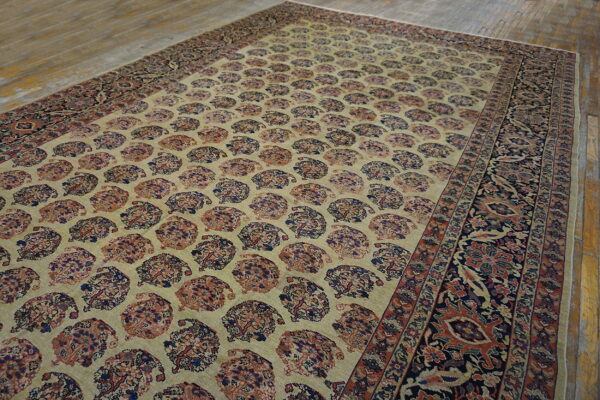 Beige rug with repeating red and navy paisley patterns and a dark floral border rests on wood planks.