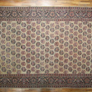 Cream and muted red rug featuring repeating medallion shapes and a dark floral border on wood flooring.