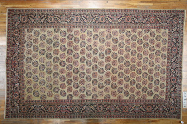 Cream and muted red rug featuring repeating medallion shapes and a dark floral border on wood flooring.