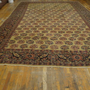 Large rug featuring a light yellow field with repetitive stylized fan motifs and an intricate navy floral border on wood floors.