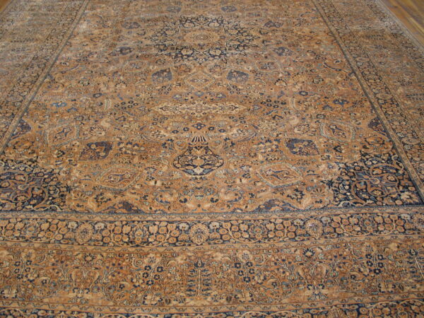 Tan and navy blue ornate rug with detailed floral patterns on a smooth wooden floor.