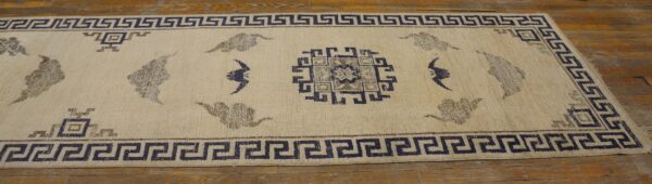 Cream runner rug featuring navy geometric borders and grey motifs rests on wood plank flooring.