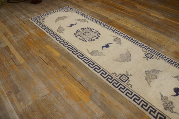 Cream runner rug featuring geometric borders and blue and gray stylized cloud patterns on distressed hardwood.