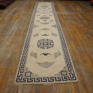 Cream runner rug with navy and gray geometric patterns rests on distressed wooden floorboards.