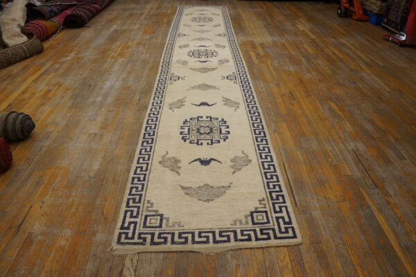 Cream runner rug with navy and gray geometric patterns rests on distressed wooden floorboards.