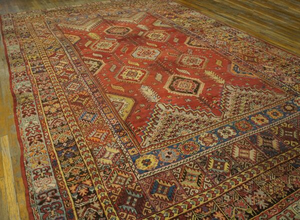 Geometric red rug with complex blue and gold borders lying on rustic light brown wooden flooring.