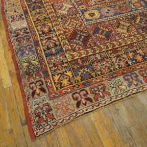 Multicolored geometric patterned rug in red, blue, and gold resting on distressed wood flooring.