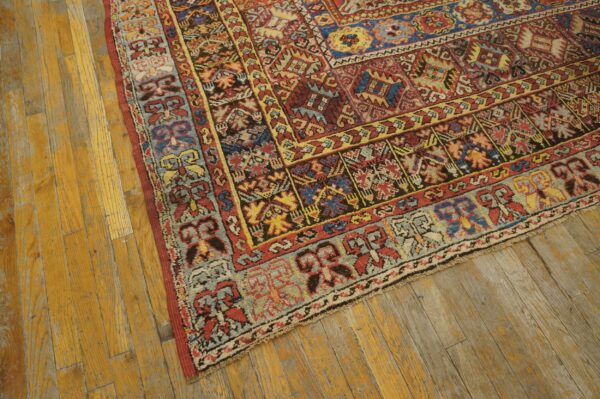 Multicolored geometric patterned rug in red, blue, and gold resting on distressed wood flooring.