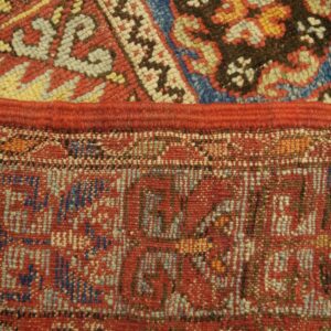 A red seam joins a high-pile blue and red geometric rug with a flatweave pattern below.