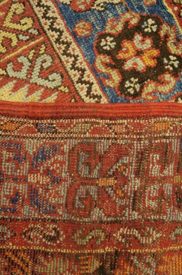 A red seam joins a high-pile blue and red geometric rug with a flatweave pattern below.