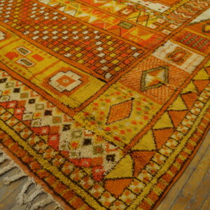 High-pile shag rug in orange, yellow, and cream geometric designs on distressed hardwood flooring.