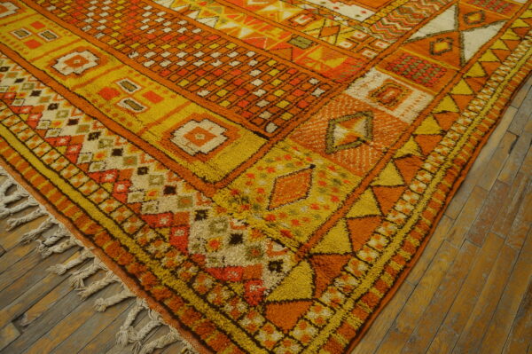 High-pile shag rug in orange, yellow, and cream geometric designs on distressed hardwood flooring.