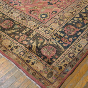 Muted rose, navy, and gold patterned rug corner with complex borders resting on wide plank wood floor.